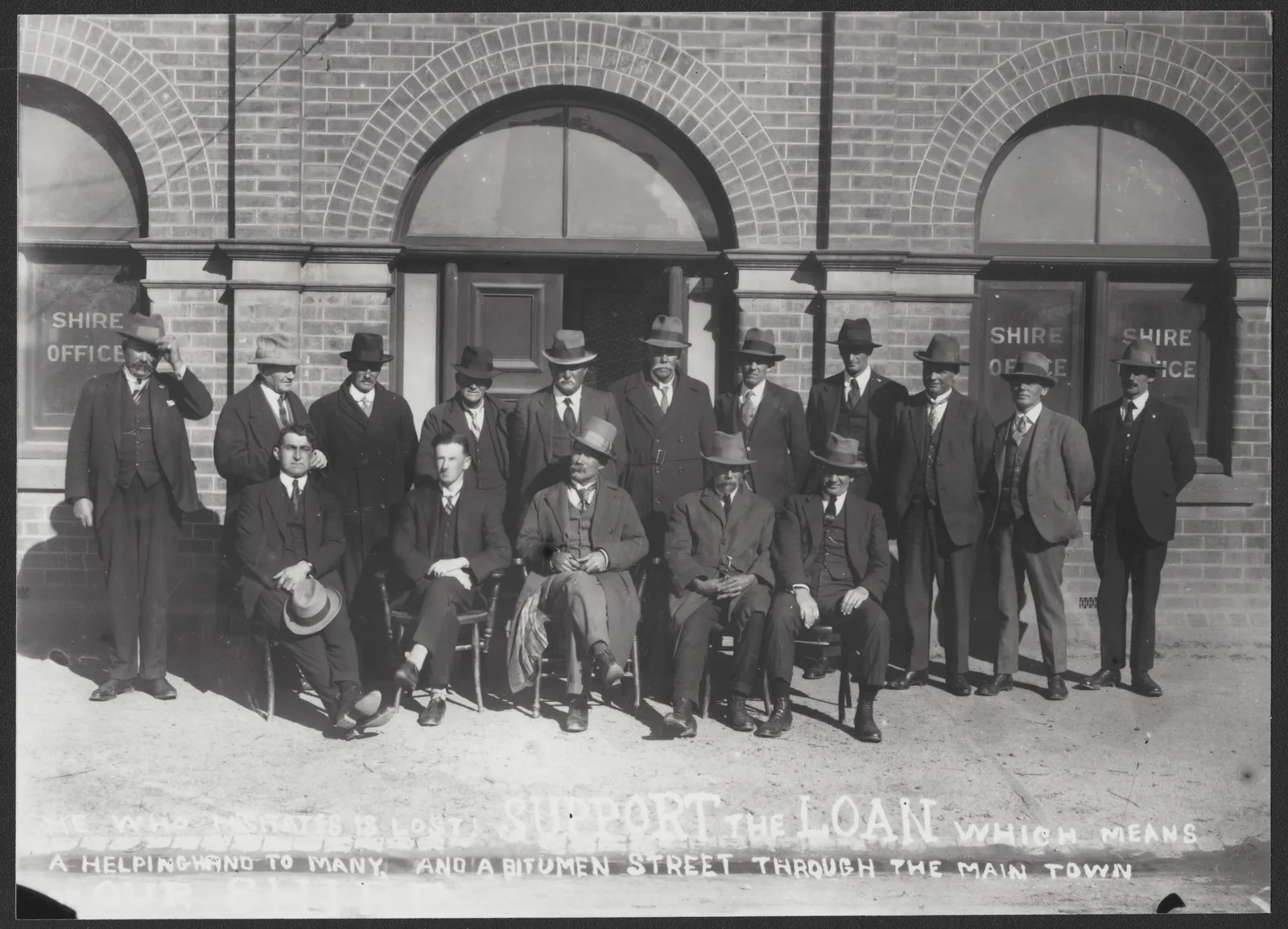 Group portrait showing men in front of a brick shire office.